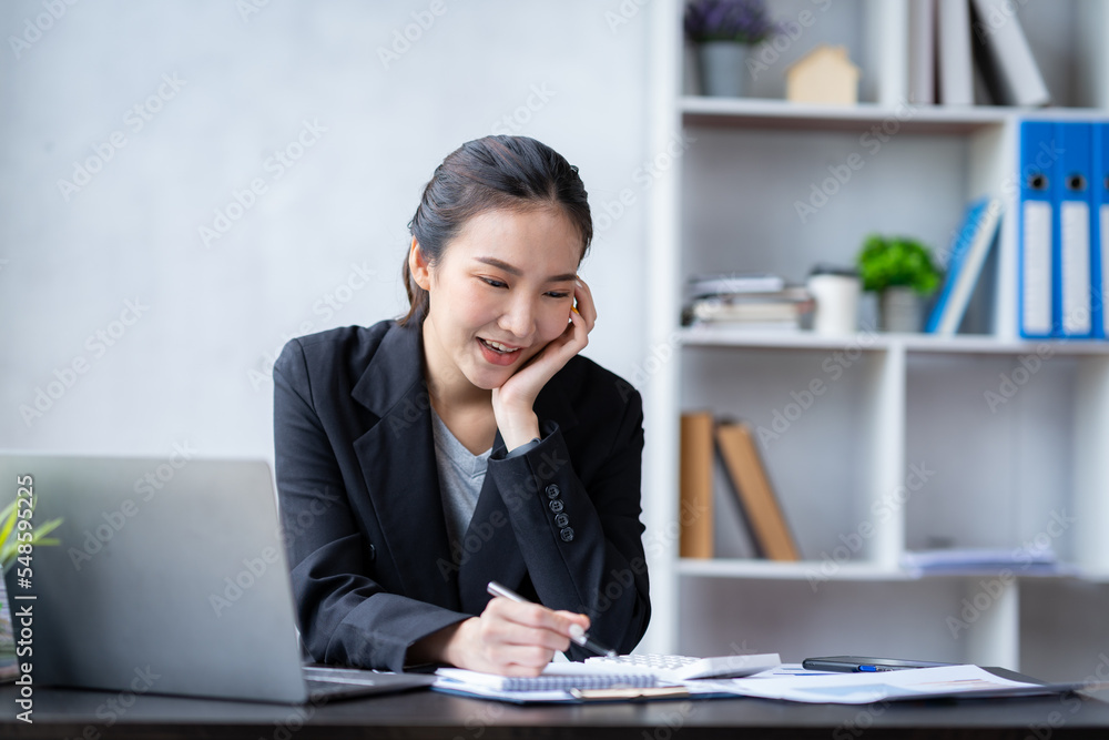 Portrait of an Asian businesswoman pressing a calculator, looking at a notebook, analyzing data, and reports, preparing presentations, marketing, and finance for sales in online shopping systems. Portrait of an Asian businesswoman pressing a calculator, looking at a notebook, analyzing data, and reports, preparing presentations, marketing, and finance for sales in online shopping systems.