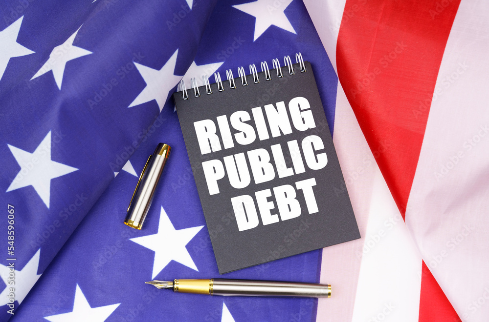 On the American flag lies a pen and a notebook with the inscription - rising public debt