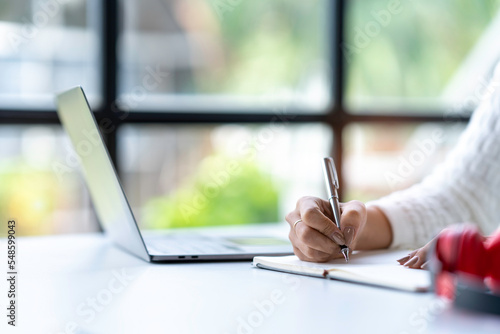 Cropped shot of Asian woman hand using laptop and writing making list taking notes in notepad working or learning on laptop educational course or training, education online concept