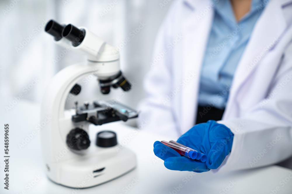 Hand of an Asian female technician wearing a lab mask or a doctor holding a vascular test and microscope with laboratory sample. Hand of an Asian female technician wearing a lab mask or a doctor holding a vascular test and microscope with laboratory sample.