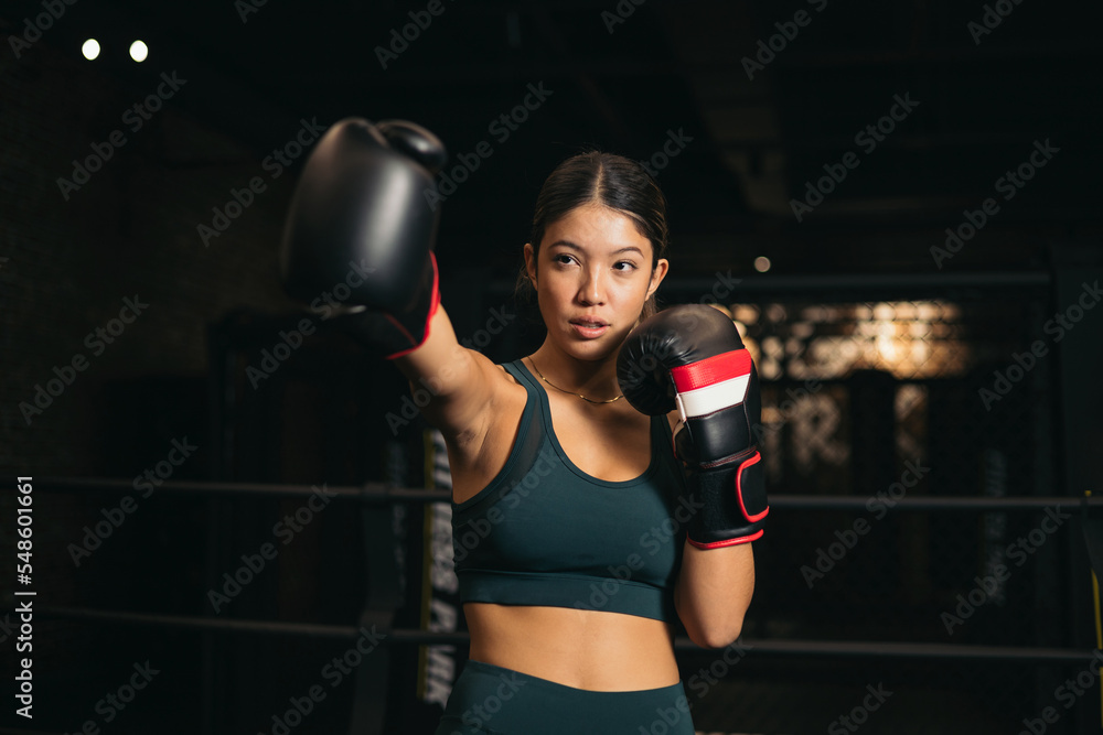 Young Asian woman punching in the air with a boxing glove. Youth boxing training, cardio exercise class.