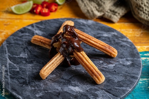 Selective shot of churros with chocolate sauce, on a round gray marble cutting board