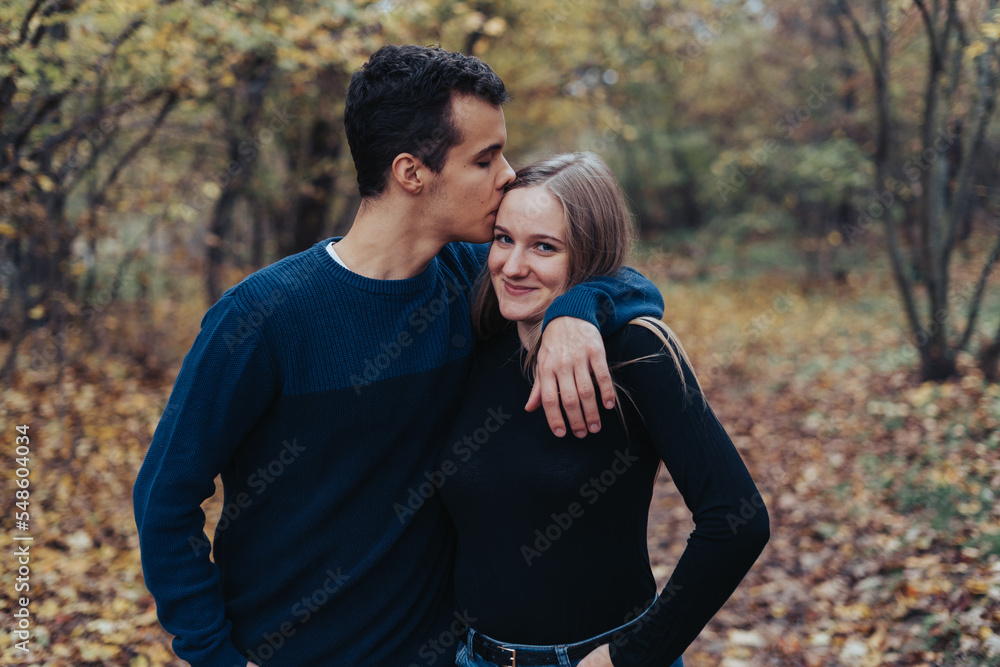 Young cheerful couple walking in a park, boyfriend kisses girlfriend Young cheerful couple walking in a park, boyfriend kisses girlfriend