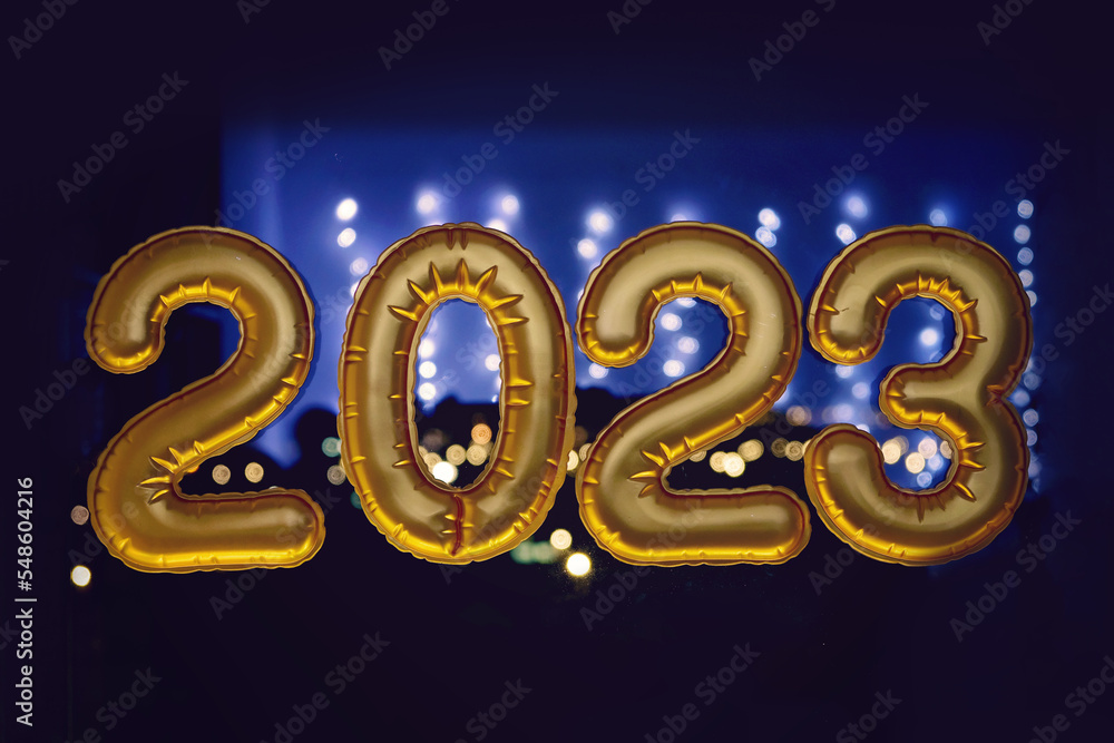 Gold inflatable foil balloons numbers 2023 on the window against the background of the night city, in neon light. New year 2023, christmas. Celebrating Christmas and New Year 2023. Gold inflatable foil balloons numbers 2023 on the window against the background of the night city, in neon light. New year 2023, christmas. Celebrating Christmas and New Year 2023.