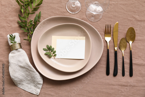Trendy table setting with blank card on beige fabric background