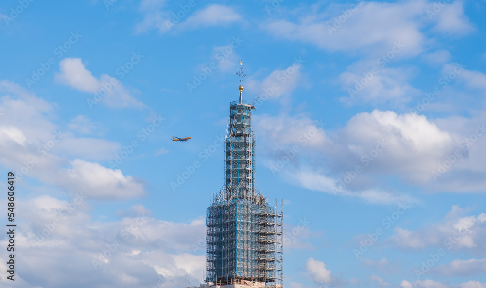A passenger plane flying over the skyscraper on a summer day.