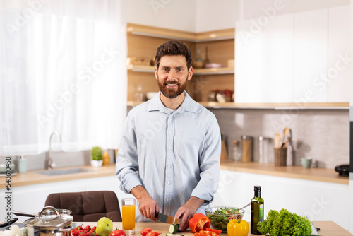 Smiling handsome adult european bearded man chef cutting organic vegetables for salad