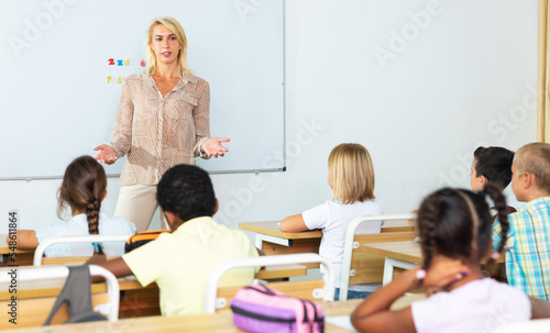 Adult female teacher is giving lecture for primary school students in the classroom