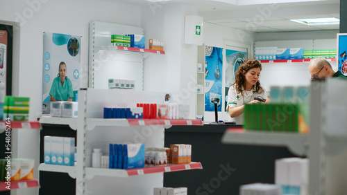 Diverse clients looking at pharmaceutical medicine on shelves, checking halthcare products to buy prescription treatment or vitamins. People in pharmacy analyzing supplement packages. Tripod shot.