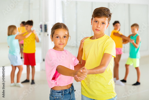 Portrait of positive tweenagers practicing slow ballroom dances in pairs in choreographic studio.