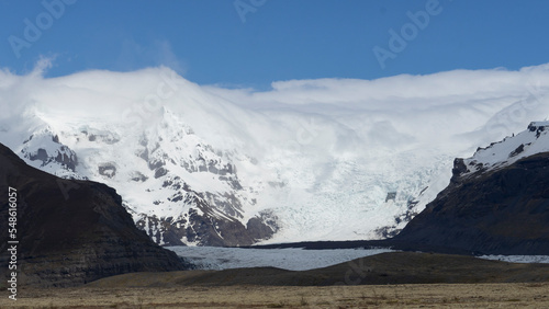Glacier landscape with clouds hanging on mountains and blue sky above. 