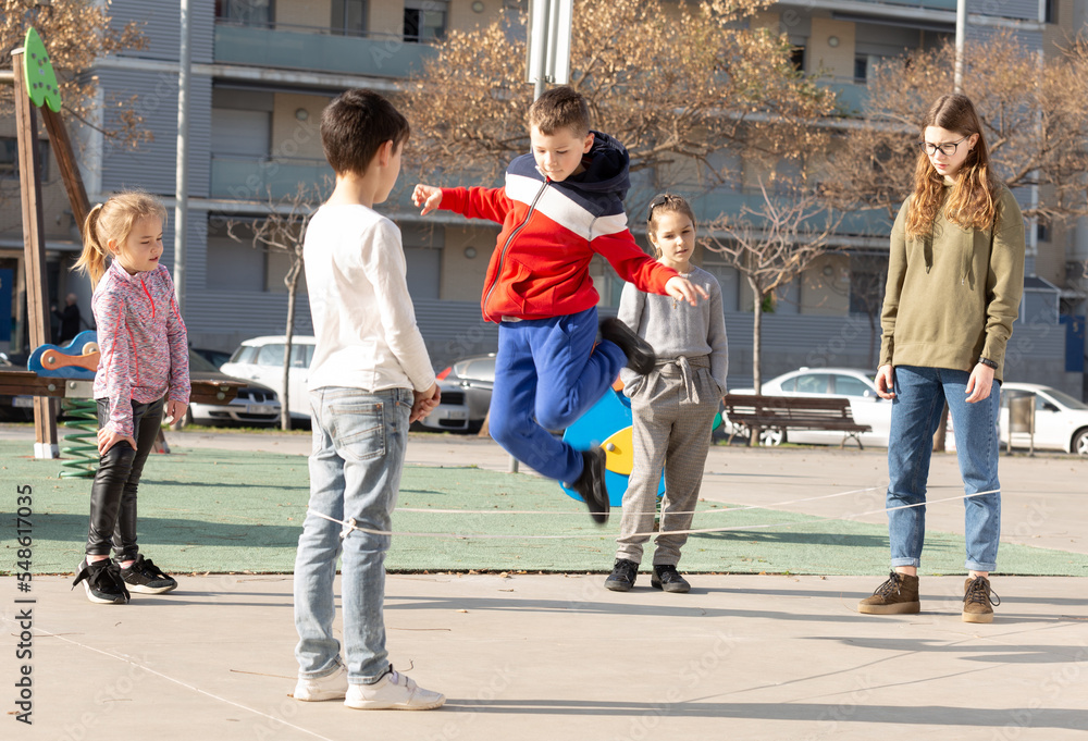 Happy smiling little friends playing with chinese jumping rope at playground. High quality photo