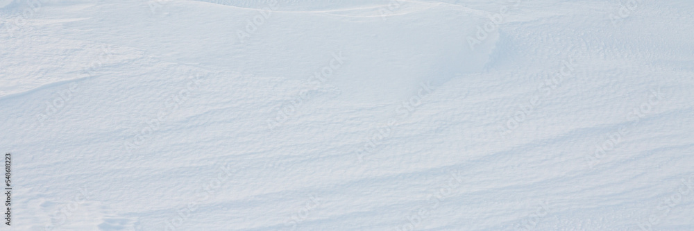 Beautiful winter background with snowy ground. Natural snow texture. Wind sculpted patterns on snow surface. Wide panoramic texture for background and design.