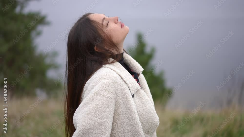 Young relaxed woman tossing hair in slow motion standing with wheat sheaf outdoors on overcast day. Portrait of confident gorgeous Ukrainian brunette lady closing eyes enjoying tranquility Young relaxed woman tossing hair in slow motion standing with wheat sheaf outdoors on overcast day. Portrait of confident gorgeous Ukrainian brunette lady closing eyes enjoying tranquility