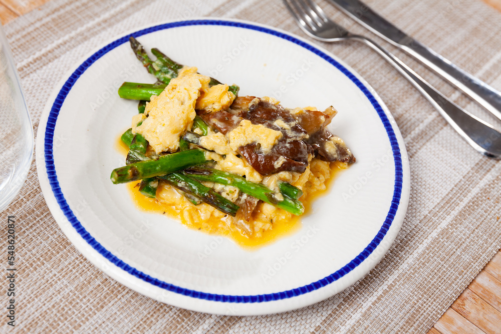 Fototapeta premium Scrambled eggs with mushrooms and asparagus served on plate with silverware.