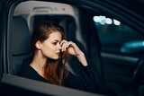a stylish, luxurious woman sits in a black car at night, touching her face with a thoughtful expression. Close horizontal photo