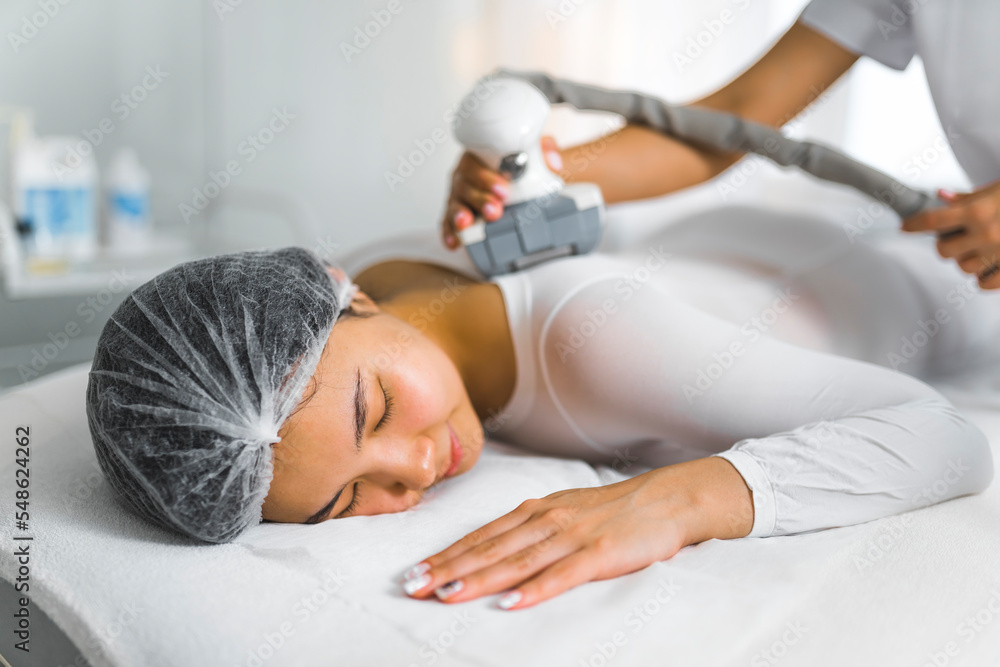 young Asian woman having procedure of anti-cellulite lpg massagein a white suit at the cosmetology clinic, side view . High quality photo young Asian woman having procedure of anti-cellulite lpg massagein a white suit at the cosmetology clinic, side view . High quality photo