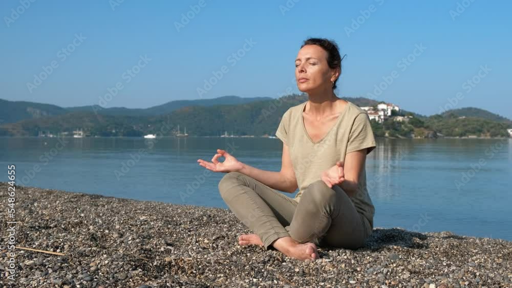 Calm zen moment on shore. A calm happy woman sits in lotus position on the pebbles shore. A concept of practicing sea yoga in the morning. Calm zen moment on shore. A calm happy woman sits in lotus position on the pebbles shore. A concept of practicing sea yoga in the morning.