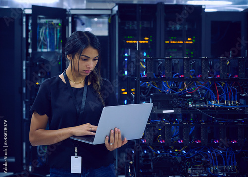 Female technician using laptop in server room
