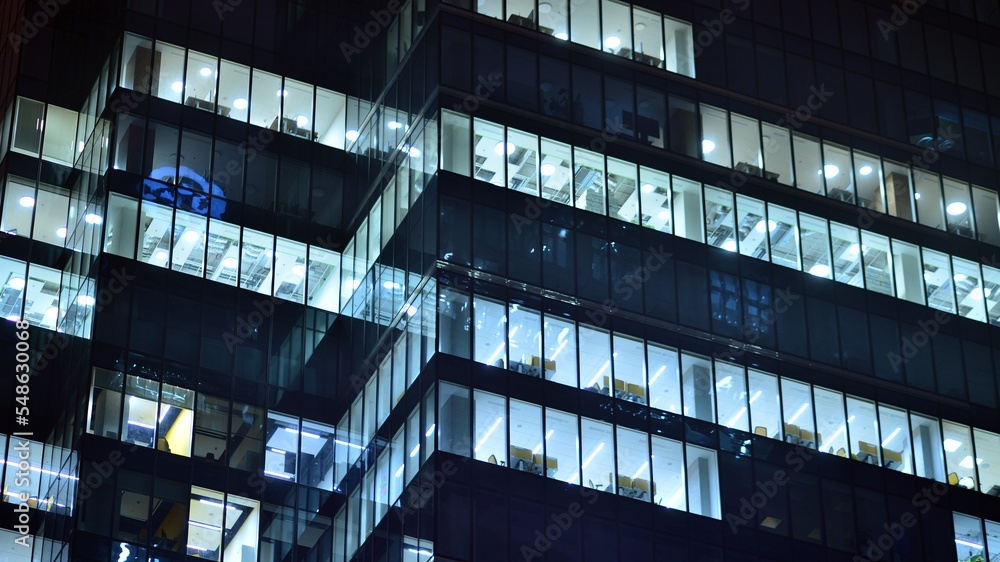 Modern office building in city at the night. View on illuminated offices of a corporate building. Blinking light in window of the multi-storey building of glass and steel. Long exposure at night Modern office building in city at the night. View on illuminated offices of a corporate building. Blinking light in window of the multi-storey building of glass and steel. Long exposure at night