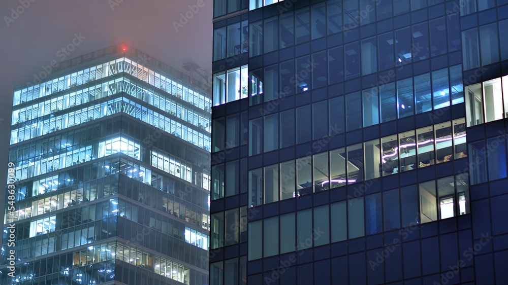 Modern office building in city at the night. View on illuminated offices of a corporate building. Blinking light in window of the multi-storey building of glass and steel. Long exposure at night Modern office building in city at the night. View on illuminated offices of a corporate building. Blinking light in window of the multi-storey building of glass and steel. Long exposure at night