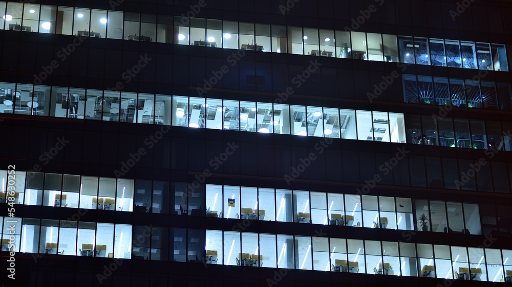 Modern office building in city at the night. View on illuminated offices of a corporate building. Blinking light in window of the multi-storey building of glass and steel. Long exposure at night Modern office building in city at the night. View on illuminated offices of a corporate building. Blinking light in window of the multi-storey building of glass and steel. Long exposure at night