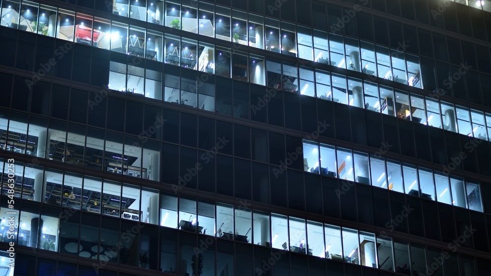 Modern office building in city at the night. View on illuminated offices of a corporate building. Blinking light in window of the multi-storey building of glass and steel. Long exposure at night Modern office building in city at the night. View on illuminated offices of a corporate building. Blinking light in window of the multi-storey building of glass and steel. Long exposure at night