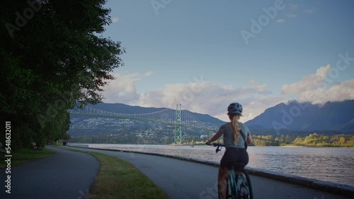 Girl biking along the seawall trail with lions gate bridge in background, vancouver