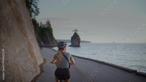 Girl biking along the seawall trail in stanley park, famous siwash rock in background photo