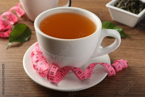 Cup of herbal diet tea and measuring tape on wooden table. Weight loss concept
