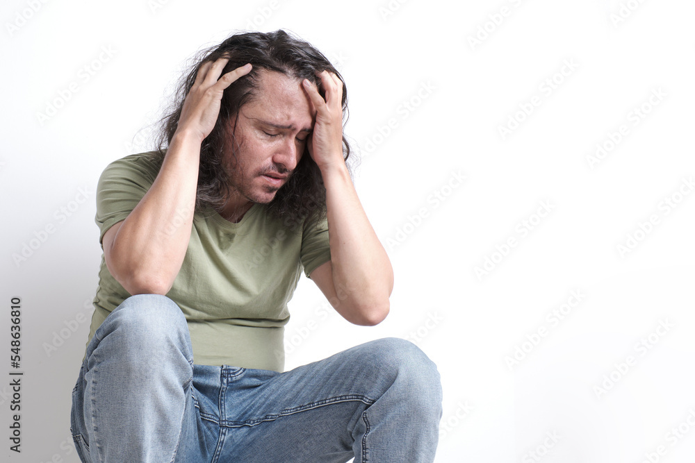 an anxious and distressed Latino man clutches his head with both hands and closes his eyes. an anxious and distressed Latino man clutches his head with both hands and closes his eyes.