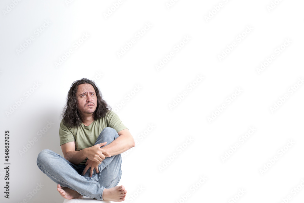 dejected, frightened and anxious disheveled Latino man sitting in a corner on a white background dejected, frightened and anxious disheveled Latino man sitting in a corner on a white background