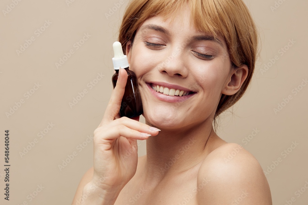 Close-up photo. Horizontal studio shot.A nice woman in a towel with white well-groomed skin, short red hair on a beige background with a new facial serum takes care of her skin. Close-up photo. Horizontal studio shot.A nice woman in a towel with white well-groomed skin, short red hair on a beige background with a new facial serum takes care of her skin.
