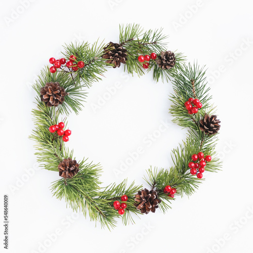 Pine christmas wreath decorated with cones and red berry fruits on white background