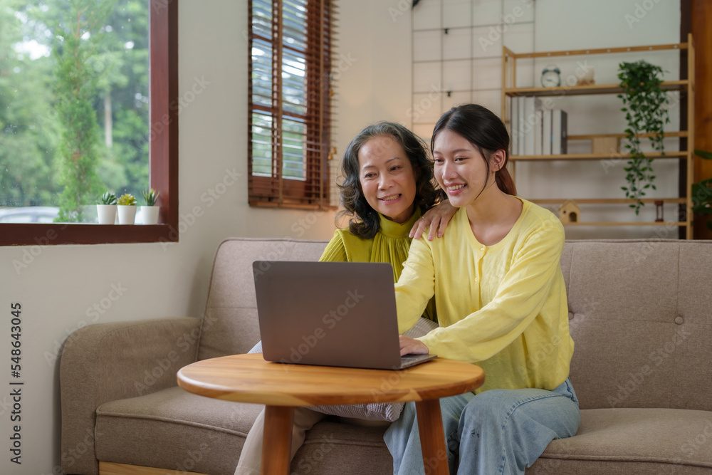 Mother-daughter duo happily uses their laptop to surf online social media together in their living room. Mother-daughter duo happily uses their laptop to surf online social media together in their living room.