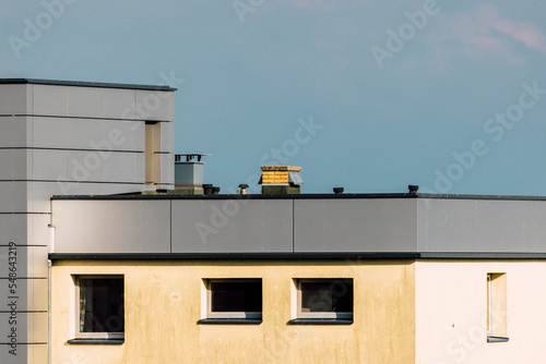 Rooftop of a modern city building with metal cladding, yellow chimney and blue sky (ID: 548643219)