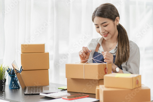 Happy woman selling products online Started as a small SME owner using a laptop computer on a table with parcels of mail in her room.