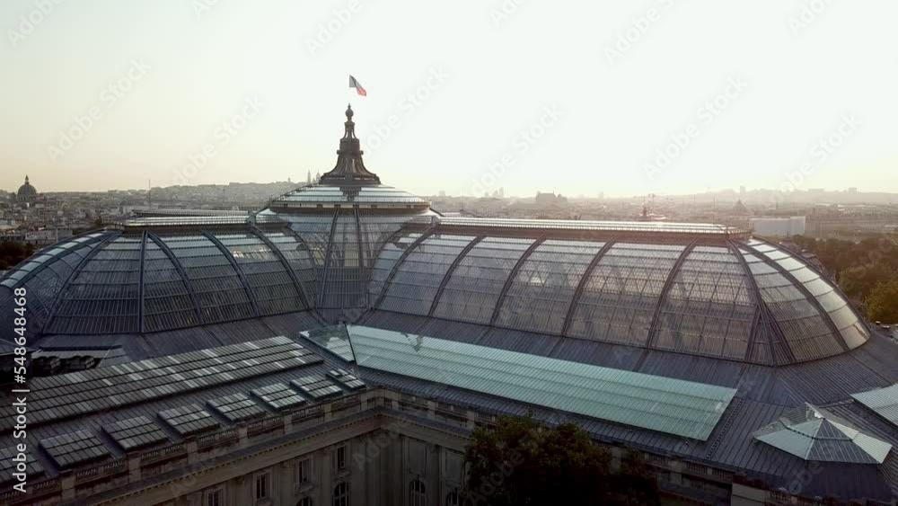Bright Cinematic aerial shot of tourist attraction of Paris, the Grand Palais with French flag waving at the top. Paris city covered with mist.