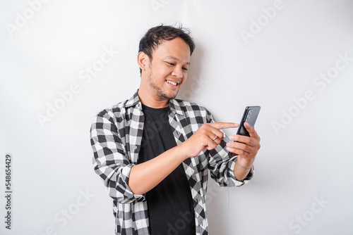 A portrait of a happy Asian man is smiling while holding on his phone, isolated by white background