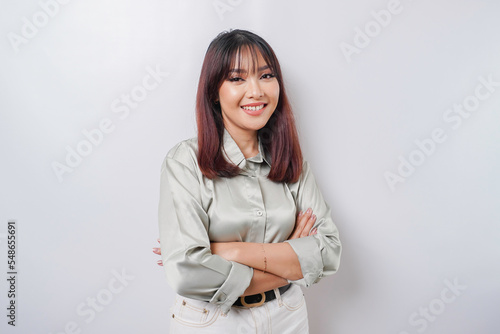 Portrait of a confident smiling Asian woman wearing sage green shirt standing with arms folded and looking at the camera isolated over white background