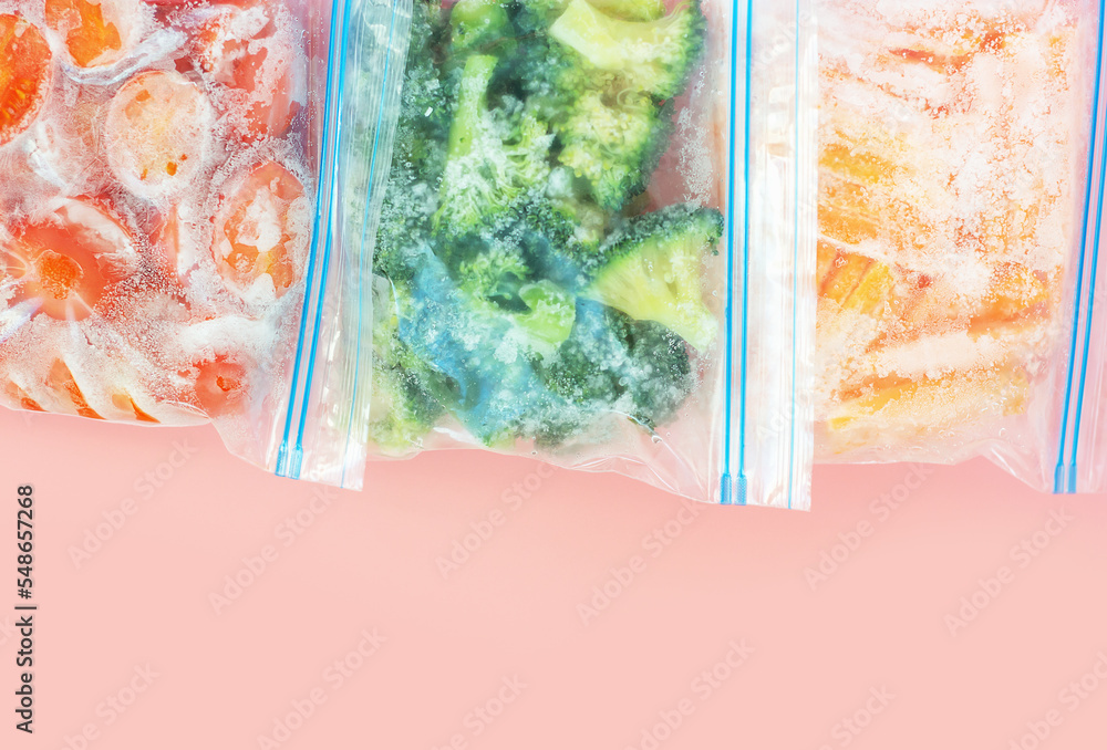 Three packages with frozen vegetables on pink background, top view