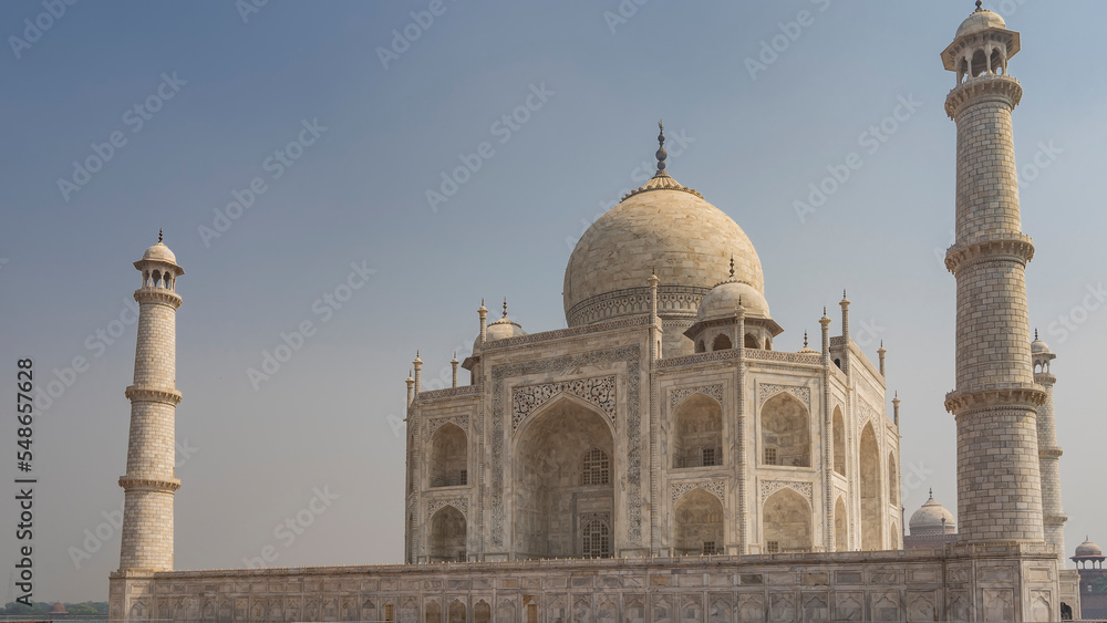 Beautiful majestic Taj Mahal against the blue sky. The ancient unique mausoleum made of white marble with domes, arches and minarets is decorated with inlays of precious stones. India. Agra