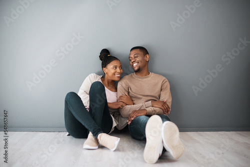 Homeowner, love and beginning with a black couple sitting together in their new home on a gray wall background. Real estate, room and mortgage with a man and woman on the floor after moving house