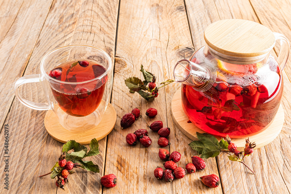 glass teapot with a decoction of freshly prepared tea with rose hips on a wooden table. vitamin useful tea for colds. glass teapot with a decoction of freshly prepared tea with rose hips on a wooden table. vitamin useful tea for colds.