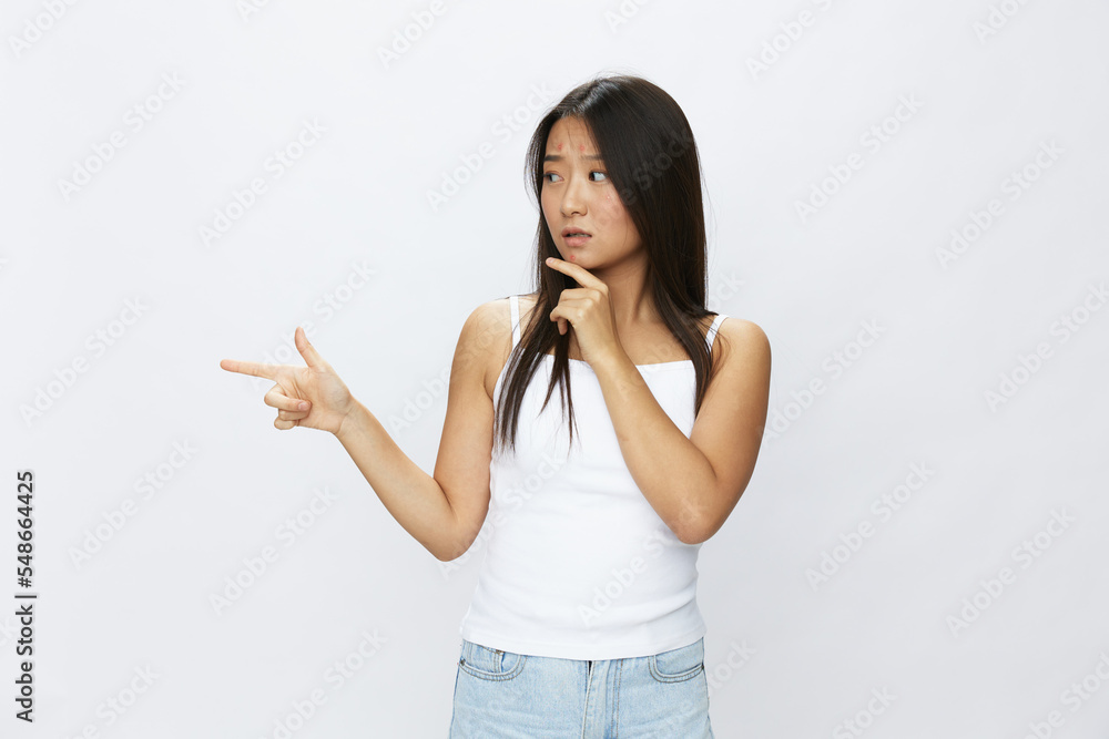 Asian woman hand signals, finger pointing facial skin problems, acne and inflammation, red rash and allergies, chicken pox, sadness from rashes. Facial skin care concept for diseases and nerves