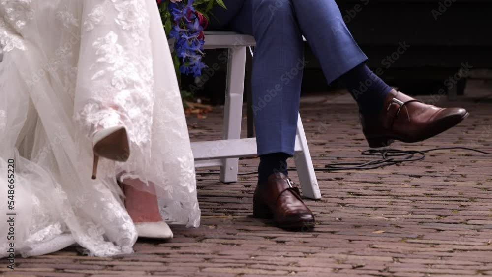 Cropped View Of The Bride And Groom Sitting On A White Chair With Legs Crossed. - Low-Level Shot Cropped View Of The Bride And Groom Sitting On A White Chair With Legs Crossed. - Low-Level Shot