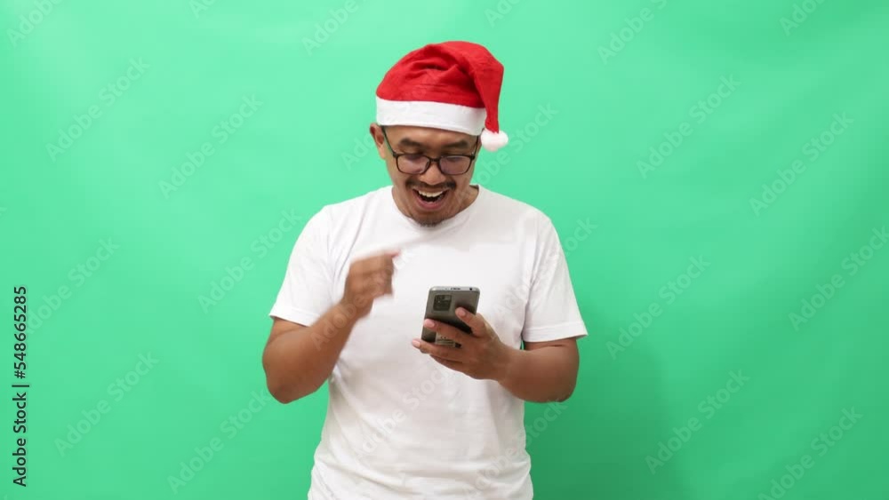Surprised asian man standing while holding a cell phone. Christmas season concept. Green screen. Surprised asian man standing while holding a cell phone. Christmas season concept. Green screen.