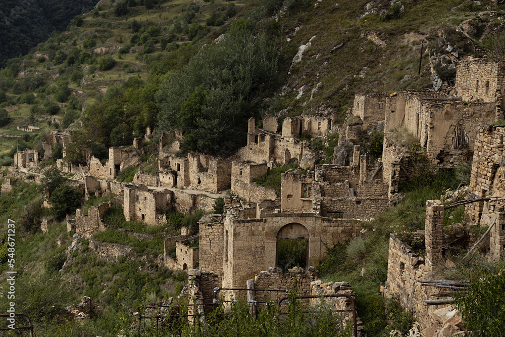 Famous aul-ghost  Gamsutl' - ruin of ancient stone city in Caucasian mountains in summer. Majestic destruction and abandoned stone castle on cliff with breathtaking canyon around and green mountains.