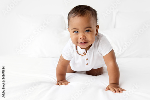 Smiling baby crawling on white bed wearing amber teething necklace photo