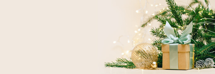 Gift box with green bow and crystal golden bauble. christmas tree and lights background, copy space. Winter holidays celebration concept.